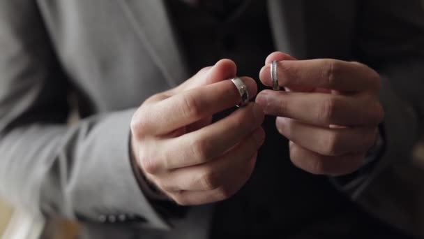 Novio en chaqueta gris sosteniendo anillos de boda en la palma de su mano, el hombre toca los anillos, cámara lenta — Vídeo de stock