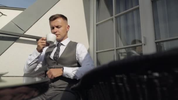 Hombre novio hombre de negocios está bebiendo café de una taza blanca en el balcón en casa en la mañana de la boda — Vídeo de stock
