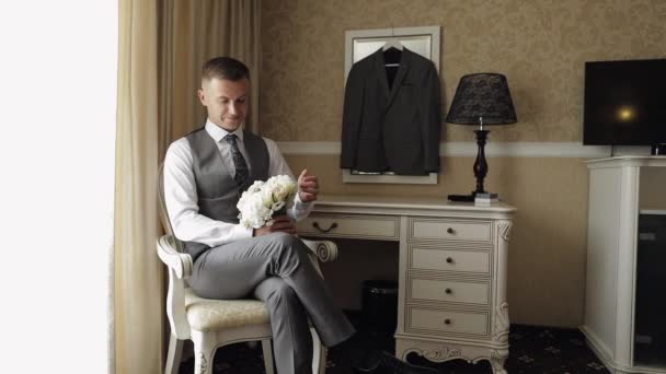 Bel homme marié avec bouquet de mariage dans ses mains à la maison près de la fenêtre se préparant à aller à la mariée — Video