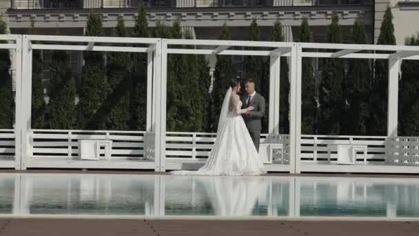 Recién casados novio novia caucásica caminando cerca de la piscina, cogidos de la mano, la familia de la pareja de boda — Vídeo de stock