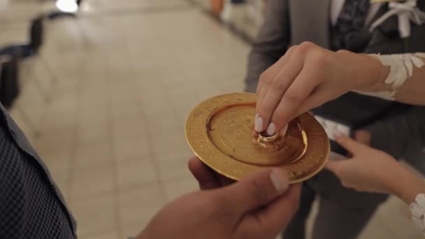 Zblízka svatebních prstenů novomanželů ve zlatém talíři se svěcenou vodou během obřadu manželského svazku — Stock video