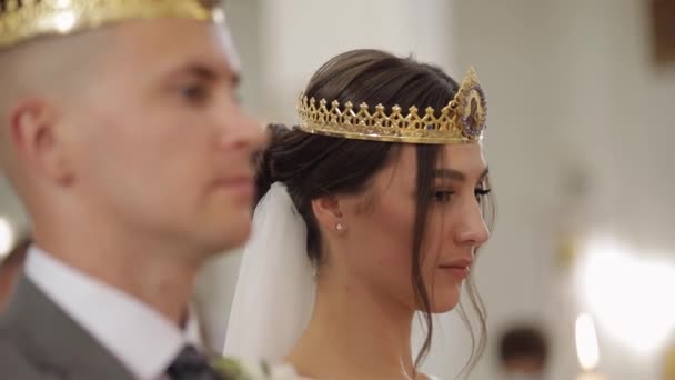 Молодята, наречена і наречений стоять у церкві в коронках, церемонії одруження — стокове відео