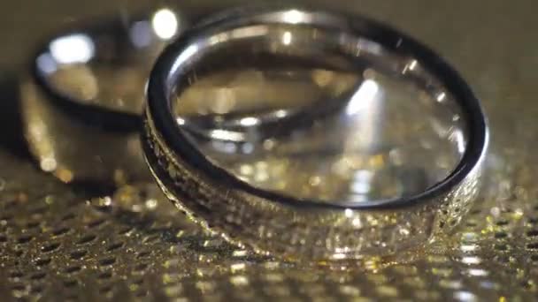 Svatební kroužky ležící, rotující, rotující na lesklém zlatém lesklém povrchu s lehkým, detailním makro — Stock video