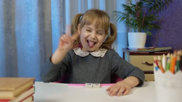 Kind meisje kijken naar webcamera maken van video bellen, studeren lessen thuis, glimlachen tonen tong — Stockvideo