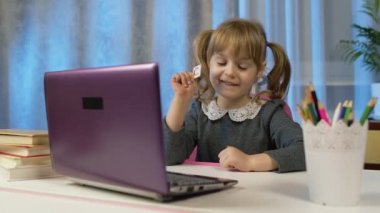 Okul ödevi yapan çocuk evde dizüstü bilgisayar ve online eğitim kullanarak deftere yazıyor.