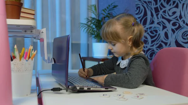 Детская девочка делает домашнее задание пишет в блокноте, с помощью ноутбука компьютер на дому, онлайн образование — стоковое фото