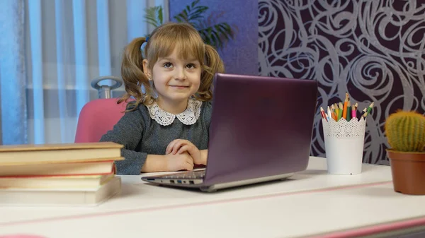 Детская девочка делает домашнее задание пишет в блокноте, с помощью ноутбука компьютер на дому, онлайн образование — стоковое фото