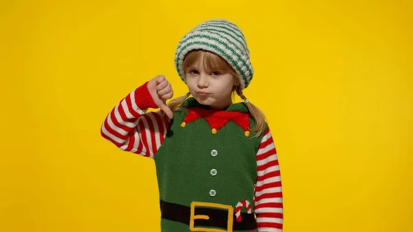 Menina criança displesed no elfo de Natal traje de Papai Noel ajuda mantém o polegar para baixo e mostra gesto de antipatia — Fotografia de Stock