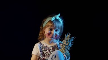 Siyah arka planda ananasın arkasına saklanan zarif genç kız gülümsüyor, oynaşıyor.