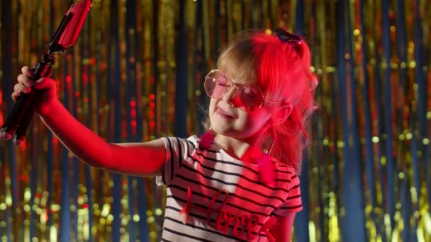 Дитячий блогер посміхається, записуючи відеоблог на смартфон у нічному клубі з червоним неоновим світлом — стокове відео