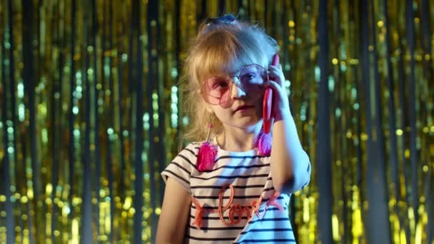 Dziewczyna w futurystycznych okularach rozmawia przez telefon komórkowy z przyjacielem w klubie nocnym z neonowym niebieskim światłem — Wideo stockowe