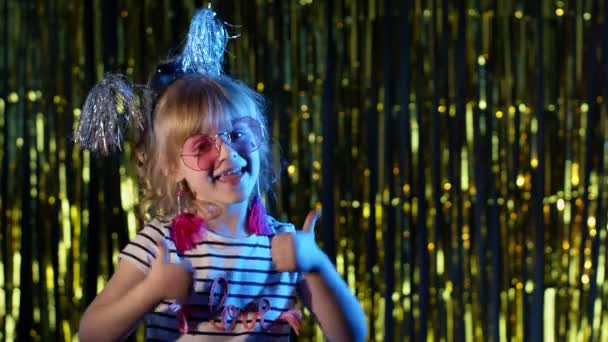 Stylish teenager kid girl standing on backlit blue neon lights and points at blank space, agree sign — Stock Video