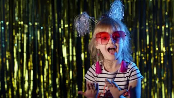 Stylish teenager kid girl standing on backlit blue neon lights and points at blank space, agree sign — Stock Video