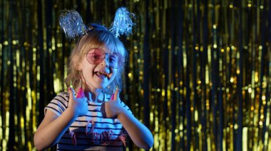 Başparmak gösteren genç bir kız, mavi ışıklı disko partisinde başarı jesti.