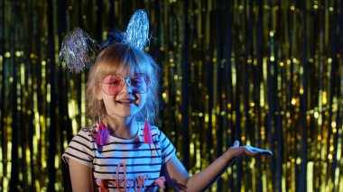 Modaya uygun gözlüklü kız mavi neon ışıklarda duruyor, boş yeri işaret ediyor, kabul.