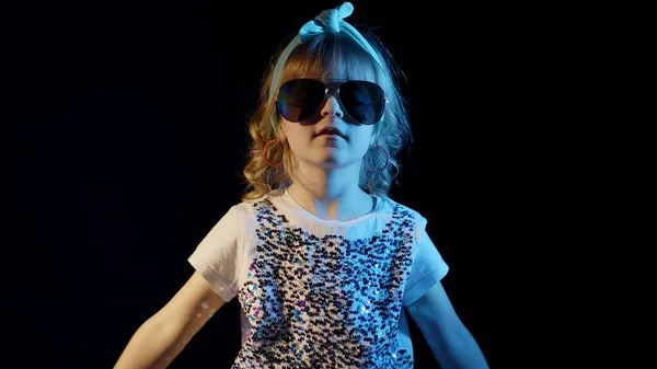 Trendiges Mädchen in futuristischer Brille tanzt, hört Musik über Kopfhörer auf schwarzem Hintergrund — Stockfoto