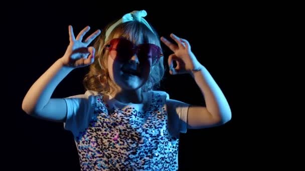 Ritratto di giovane ragazza bionda in brillante luce colorata al neon raggi mostrando segno ok su sfondo nero — Video Stock