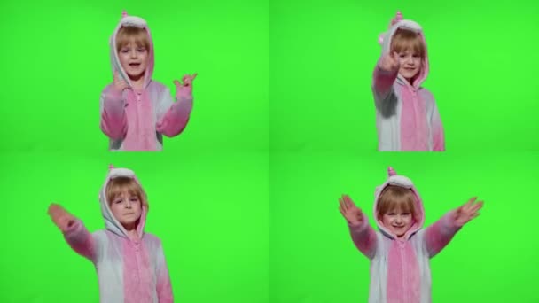 Маленька дівчинка посміхається, махає привітанням, привітається або прощається з рукою в єдинорігній піжамі на клавіші хроми — стокове відео
