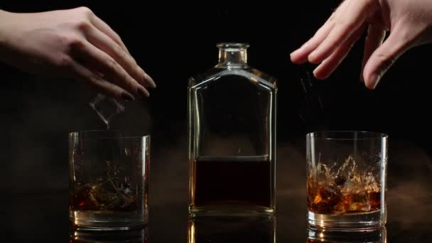 Två händer med glas konjak whisky med isbitar gör skål toast på svart bakgrund — Stockvideo