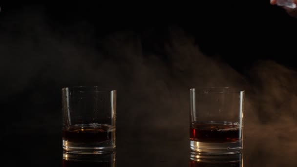 Barmans soltando cubos de gelo em copos com uísque, conhaque, conhaque em fundo preto — Vídeo de Stock