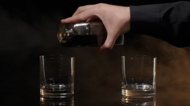 Barman pour golden whiskey, cognac, brandy, bourbon, rum from bottle into glasses on dark background — Stock Video