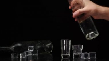 Barmen siyah arka planda bardaklara buz küpleriyle iki shot votka dolduruyor.