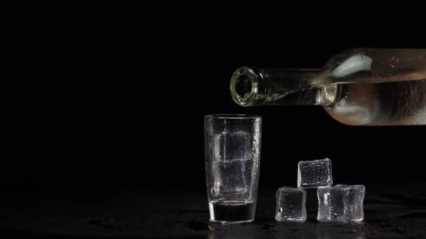 Barkeeper gießt Schuss Wodka mit Eiswürfeln aus Flasche in Schnapsglas auf schwarzem Hintergrund — Stockvideo