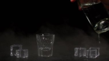 Barmen, siyah arka planda buzlu votka kadehini shot bardağına dolduruyor.
