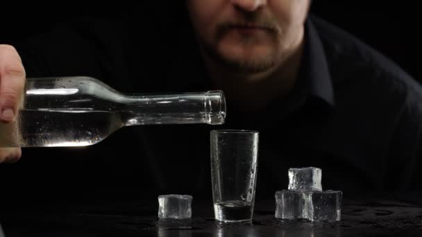 Бармен наливает замороженную водку из бутылки в рюмку со льдом кубиками на черном фоне — стоковое видео