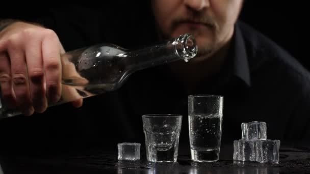 Alcoholische man gieten van bevroren wodka uit fles in shot glas met ijsblokjes op zwarte achtergrond — Stockvideo