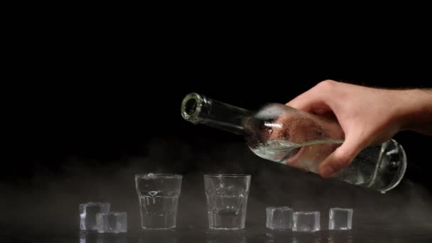 Dos manos con vasos de vodka haciendo vítores, levantando tostadas sobre fondo negro con cubitos de hielo — Vídeos de Stock