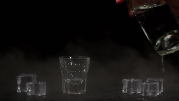 Barman gieten van shot van wodka met ijsblokjes uit fles in shot glas op zwarte achtergrond — Stockvideo