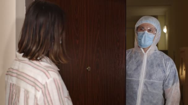 Frau öffnet Tür für Arzt im PSA-Anzug, Impfung gegen Coronavirus — Stockvideo