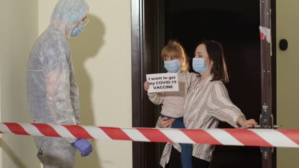 Doctor in protective suit with vaccine ampoule and syringe visiting mother with daughter at home — Stock Video
