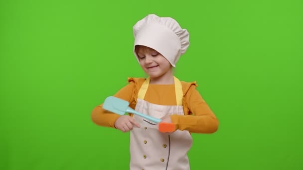 Barn flicka klädd i förkläde som kock kock dans spatel på kroma nyckel bakgrund, slow motion — Stockvideo