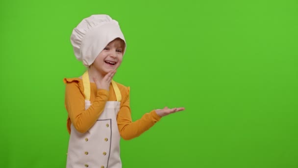 Niño niña vestida cocinero en delantal apuntando a la derecha en el espacio en blanco en croma clave fondo — Vídeos de Stock