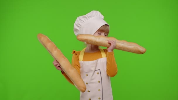 Niña cocinera cocinera panadera en delantal y sombrero olfateando dos baguettes, tonteando, haciendo caras — Vídeos de Stock