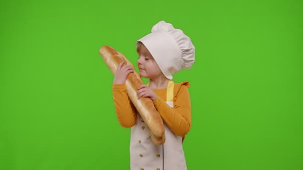 Παιδί κορίτσι ντυμένος μάγειρας σεφ δείχνει μυρίζοντας δύο φρέσκιες μπαγκέτες, τεντώνει το ψωμί στην κάμερα — Αρχείο Βίντεο