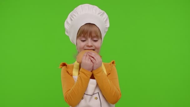 Девочка 5-6 лет, одетая в фартук, как повар, ест вкусный бутерброд на хромовом ключе — стоковое видео