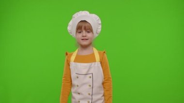 Çocuk çocuk aşçı aşçı aşçı poz veren, gülümseyen, yeşil renkli anahtar arka planında baş parmağını gösteren
