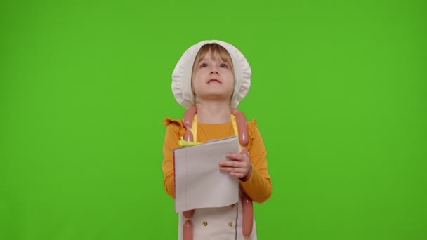 Дитяча дівчинка готує шеф-кухаря з ручкою в блокноті новий рецепт, що стоїть над ключовим фоном хрому — стокове відео