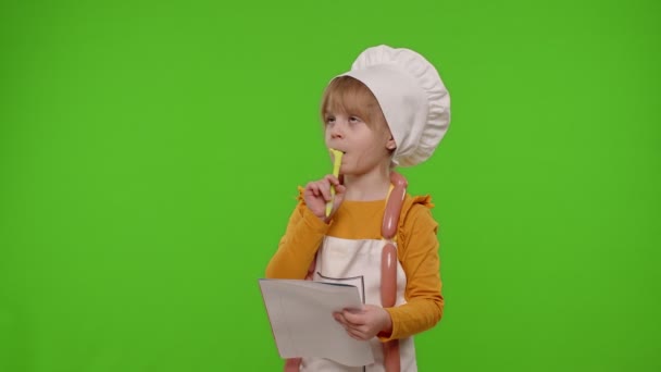 Kind meisje kind kok chef-kok schrijven met pen in notebook nieuw recept staande over chroma key achtergrond — Stockvideo