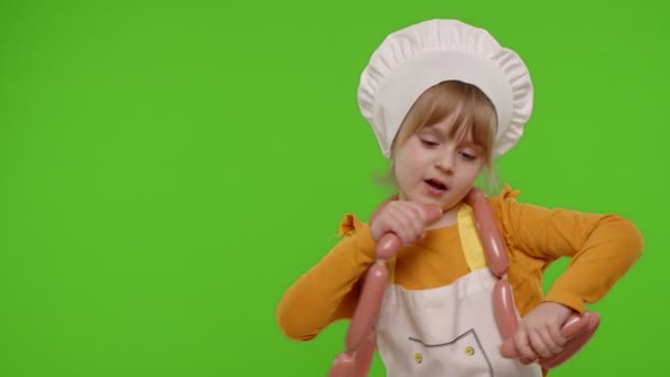 Nastoletnie dziecko dziewczyna przebrana za kucharza w fartuchu taniec z kiełbaskami, wygłupiając się na klawisz chroma — Wideo stockowe