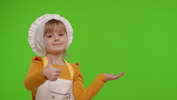 Niño niña vestida cocinero en delantal apuntando a la derecha en el espacio en blanco en croma clave fondo — Vídeos de Stock