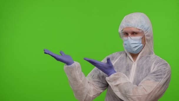 Medico in tuta protettiva PPE che punta a sinistra sullo spazio vuoto su sfondo cromatico chiave — Video Stock