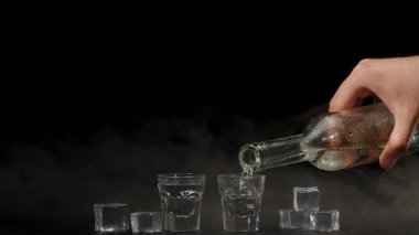 Barmen siyah arka planda bardaklara buz küpleriyle iki shot votka dolduruyor.