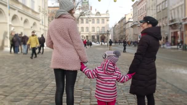 Лесбійські подружжя туристів, які тримаються за руки з усиновленням дитини, залишаються на зимовій вулиці центру міста. — стокове відео