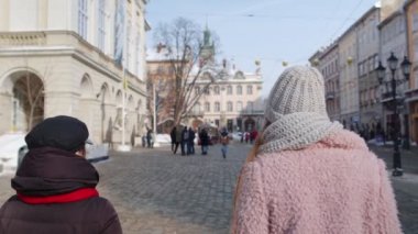 İki gülümseyen lezbiyen lezbiyen LGBT turistleri şehir sokaklarında birlikte yürüyorlar, aile çiftleri kucaklaşıyorlar.