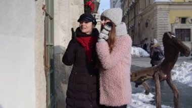 İki gülümseyen kadın turist şehir caddesinde vitrinlere bakıyor, aile çiftleri konuşuyor, kucaklaşıyorlar.