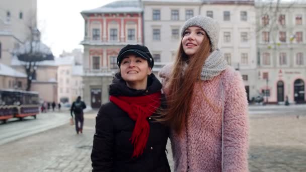 Две улыбающиеся женщины-сестры-туристки идут вместе по городской улице, семейная пара разговаривает, обнимает — стоковое видео